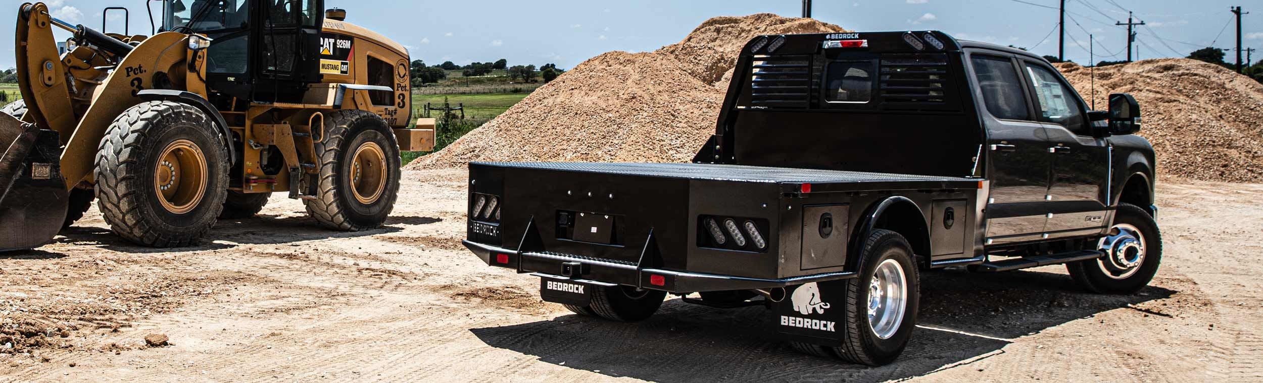Bedrock Granite Series steel flatbed on a black dually at a construction site with CAT loader